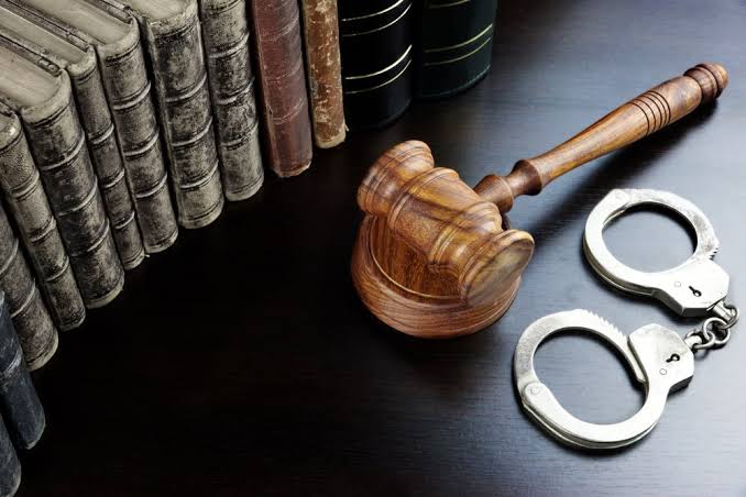 A wooden gavel and metal handcuffs rest on a dark desk next to a row of old law books, representing the legal representation provided by a DUI Charge Defense Attorney.