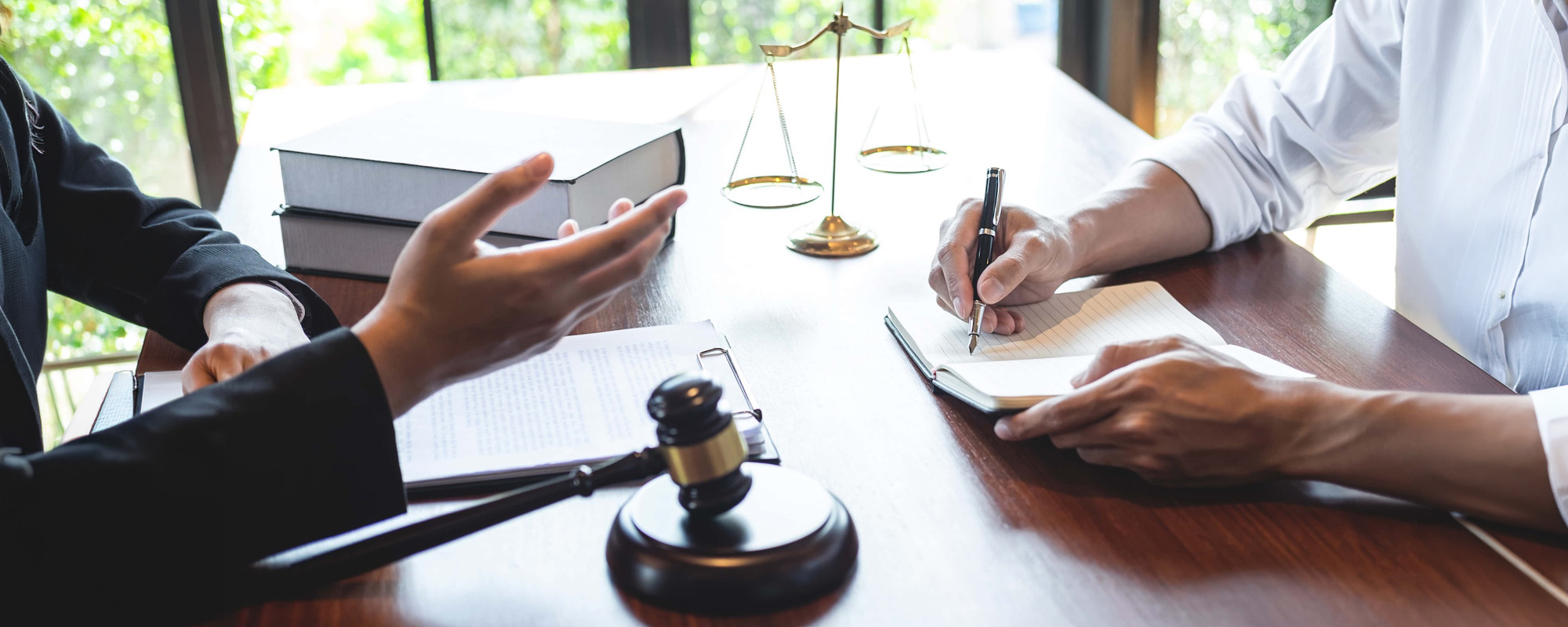 An attorney speaking with a client who is taking notes at a desk with a gavel and scales of justice, representing DUI Lawyer Gaylord MI services.
