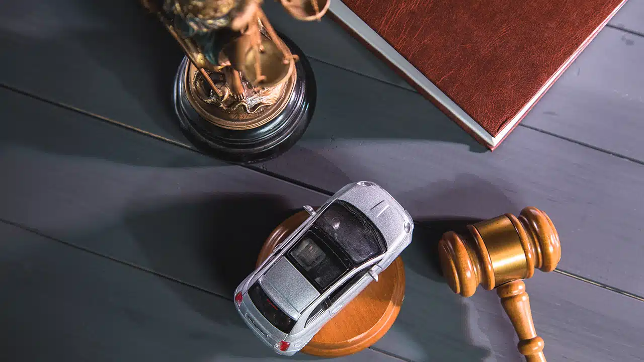 A top-down view of a miniature car next to a wooden gavel and Lady Justice statue on a desk, representing DUI Legal Representation Charlevoix services.