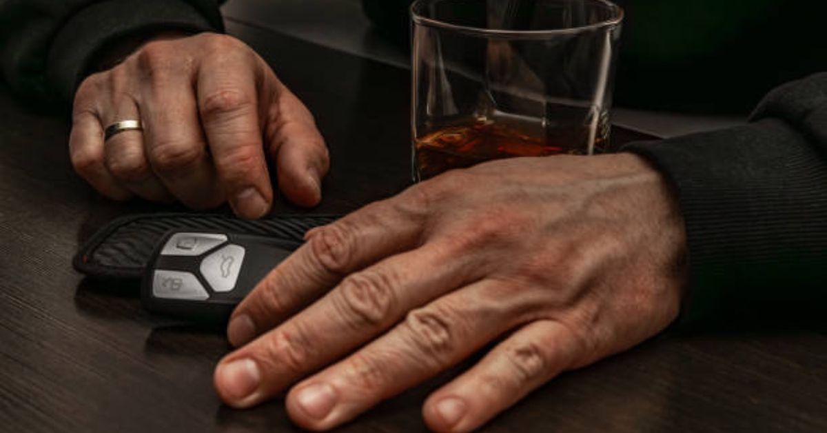 A person's hands next to a car key fob and a glass of alcohol on a table, representing DUI Legal Representation Charlevoix services.