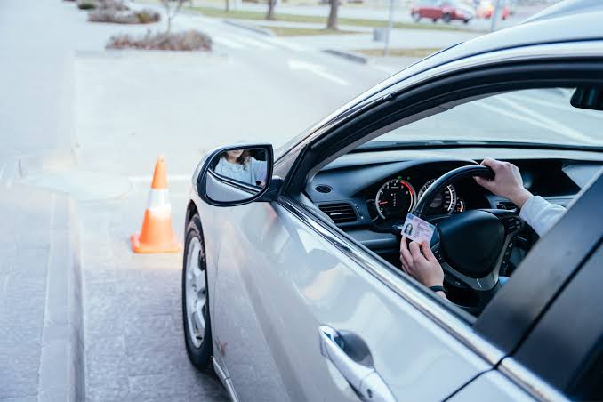 A driver holding up a driver's license behind the wheel of a car, representing driving privileges regained with a DUI License Restoration Lawyer.