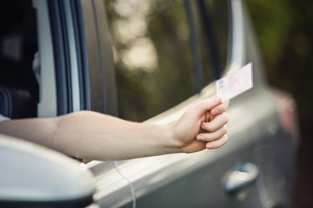 A person holding a driver's license out of a car window, representing driving privileges reinstated with the help of a DUI License Restoration Lawyer.