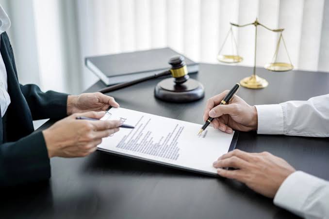 A client signing legal documents across from a DUI License Restoration Lawyer at a desk with a gavel and scales of justice.