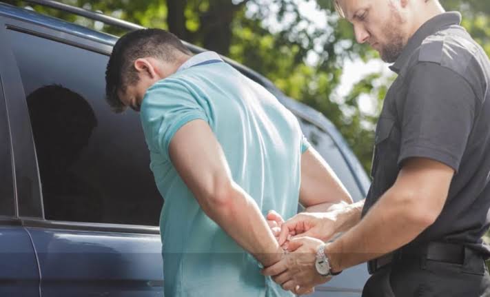 A police officer handcuffing a driver next to a vehicle, representing Drunk Driving Defense Gaylord legal services.