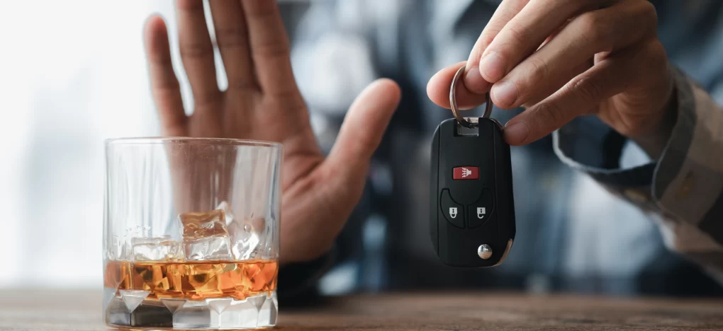 A hand holding car keys next to a glass of whiskey, representing Drunk Driving Defense Gaylord services.