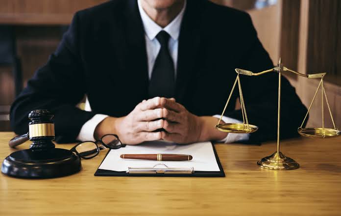 An attorney sitting at a desk with hands clasped alongside a gavel and scales of justice, representing OWI Lawyer Gaylord MI services.