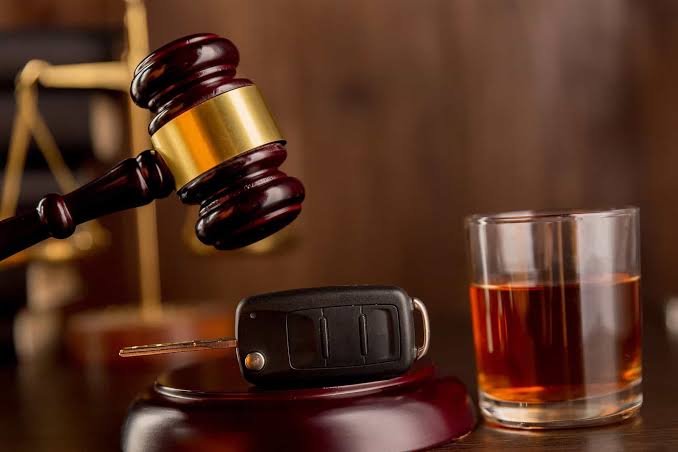 A wooden judge's gavel striking a sounding block next to a car key fob and a glass of whiskey, symbolizing legal representation for Criminal DUI Defense Gaylord.