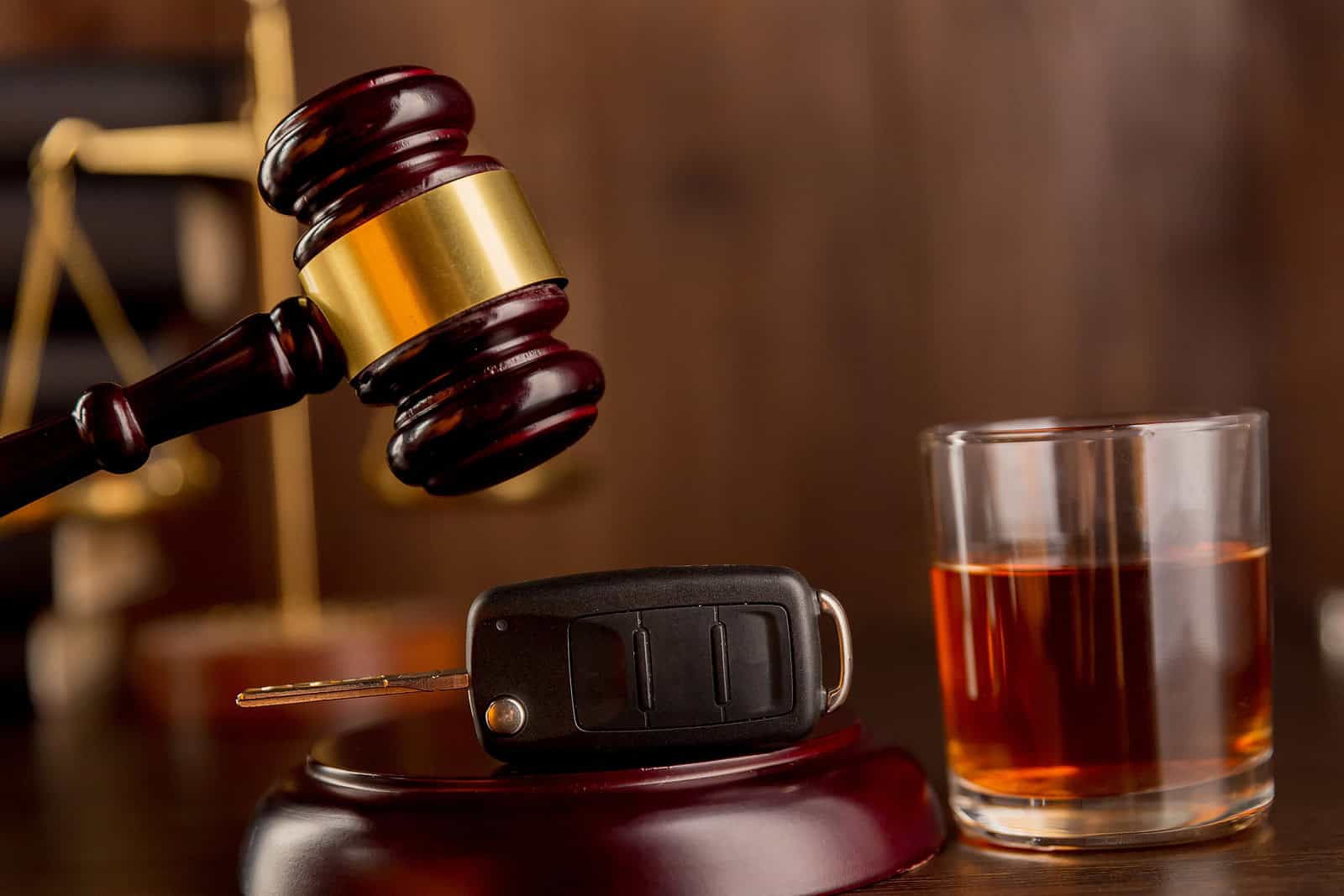 A car key and a glass of whiskey sitting beside a wooden judge's gavel, symbolizing legal cases handled by a DUI Criminal Defense Attorney.
