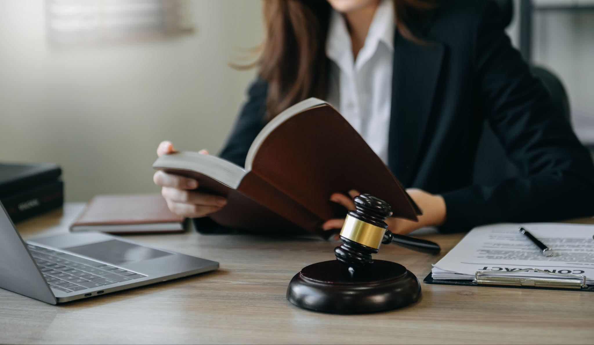 Female attorney reading a law book at a desk set with a gavel, laptop, and legal contracts, working as a DWI Criminal Defense Attorney.