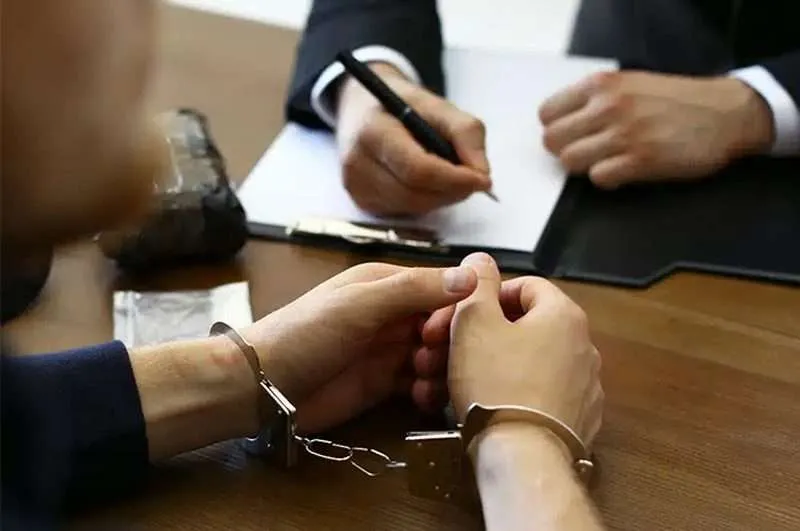 Handcuffed client sitting across a desk during a legal consultation with a DWI Criminal Defense Attorney taking notes on paperwork.