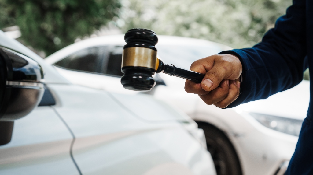 A hand holding a gavel over a car, representing defense from a First Offense OWI Lawyer.