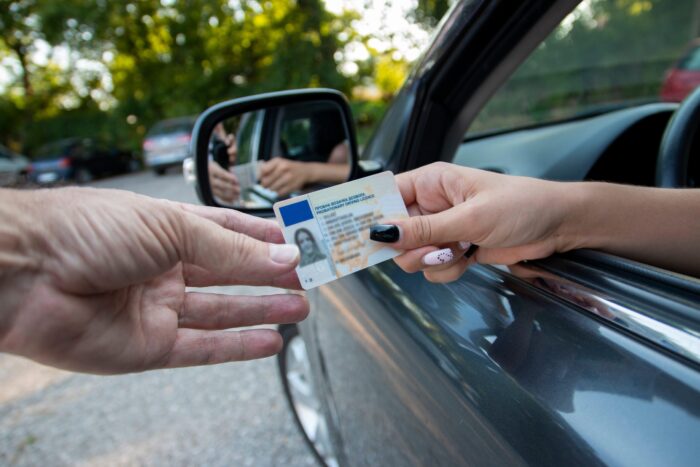 Driver handing over a driver's license through an open car window during a traffic stop, illustrating representation for License Suspension Defense Grayling.