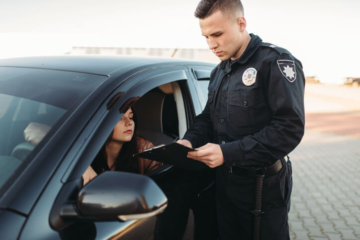 Police officer issuing a traffic ticket to a driver seated in a black car, highlighting scenarios requiring License Suspension Defense Grayling.