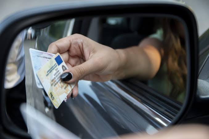 Close-up view reflected in a side mirror of a driver handing over identification cards during a traffic stop, representing legal help for License Suspension Defense Grayling.