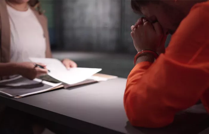 A distressed defendant wearing an orange prison jumpsuit and handcuffs sits with head bowed at a consultation table across from an attorney reviewing legal papers, illustrating a critical case review with a dedicated Felony DUI Defense Attorney.