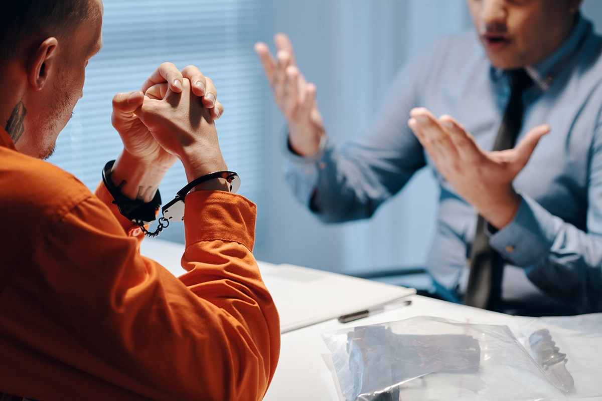 A handcuffed individual in an orange jumpsuit sits across a table talking with a professional consultant, highlighting a critical case strategy session with a dedicated Felony DUI Defense Attorney.
